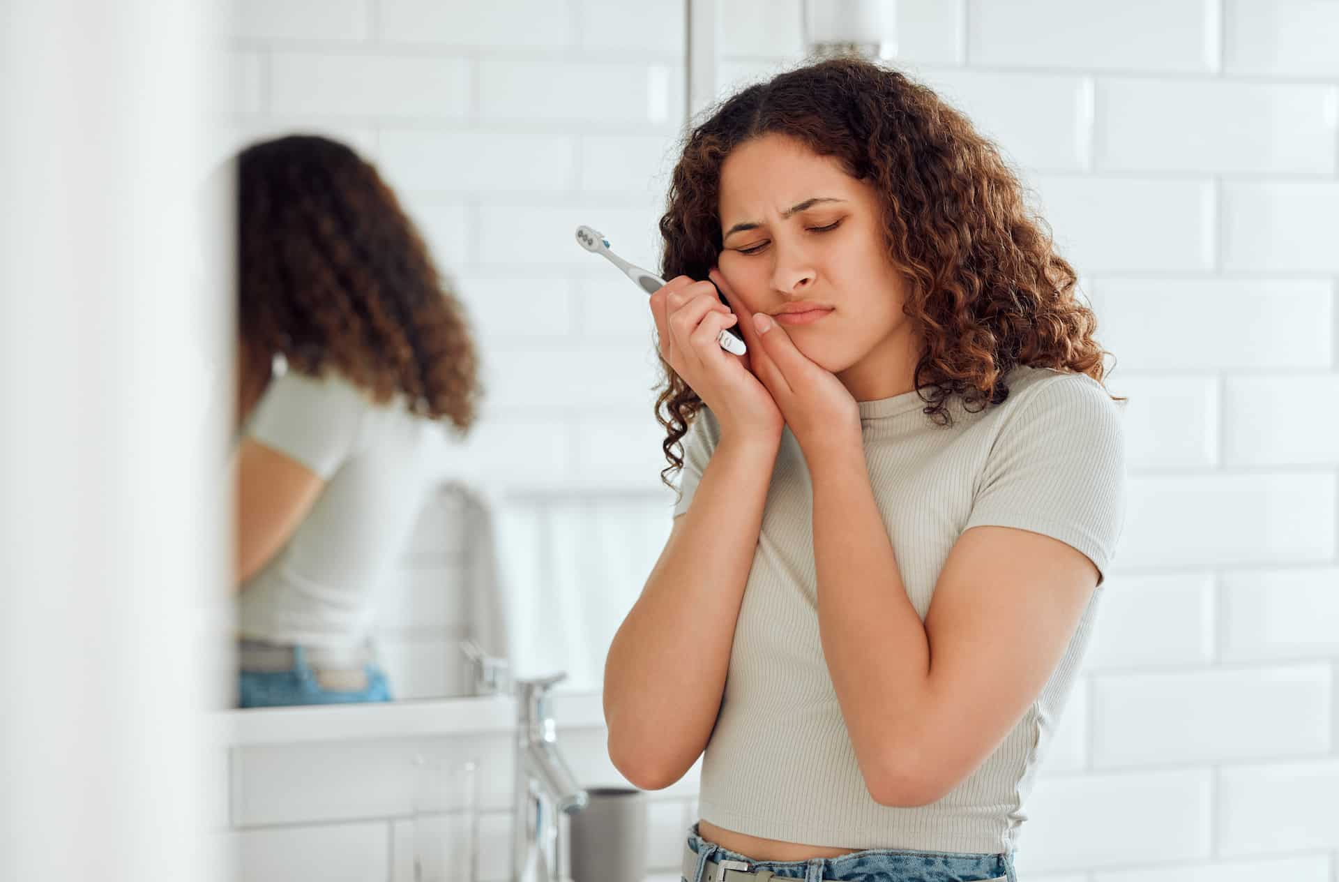 A woman with sensitive teeth is brushing her teeth in the bathroom