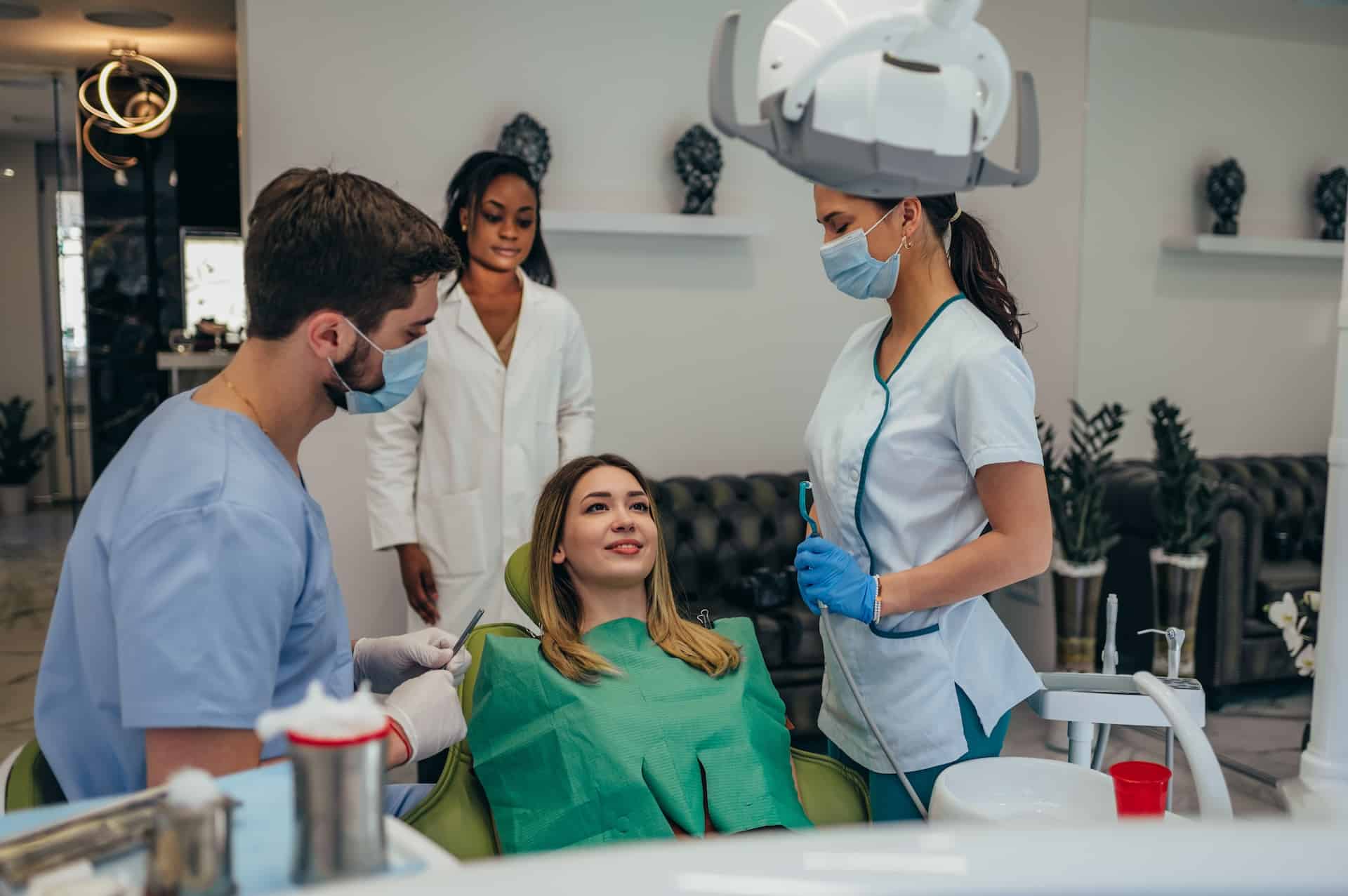 dentist and an assistant wearing masks and gloves prepare to examine her for a possible dental crown